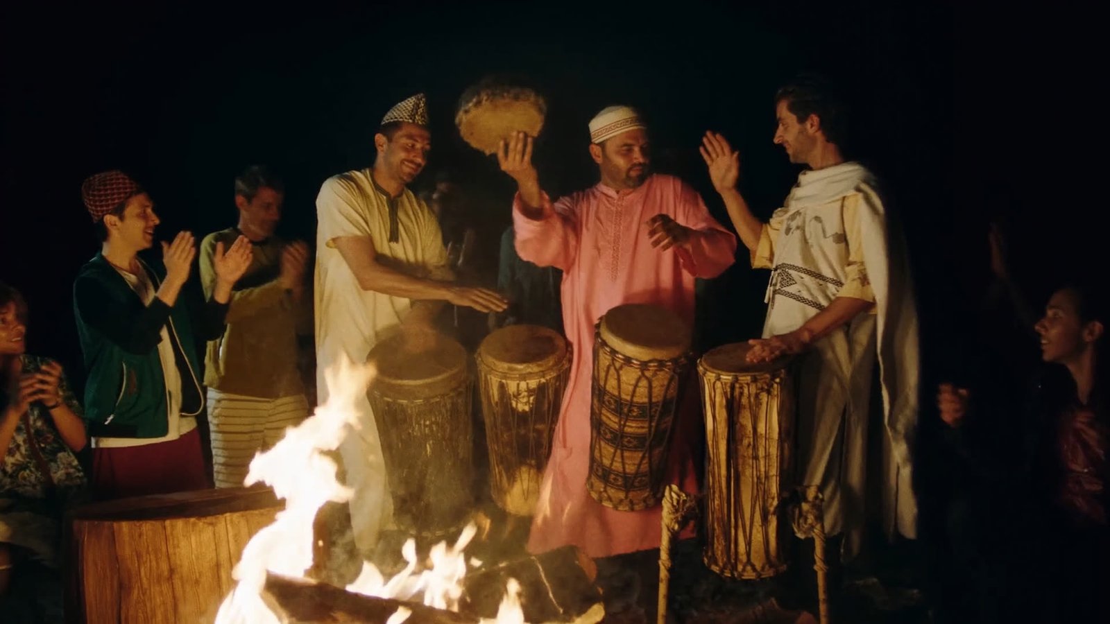 Local musicians playing traditional drums around a campfire, travelers clapping