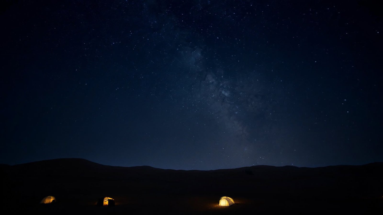 The Milky Way over Erg Chegaga with tents glowing softly below