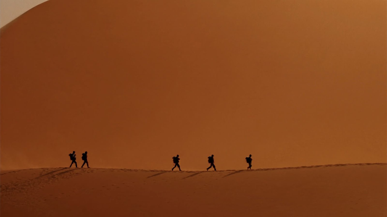 Hikers walking the ridgeline of towering Erg Chegaga dunes, tiny against the sand sea